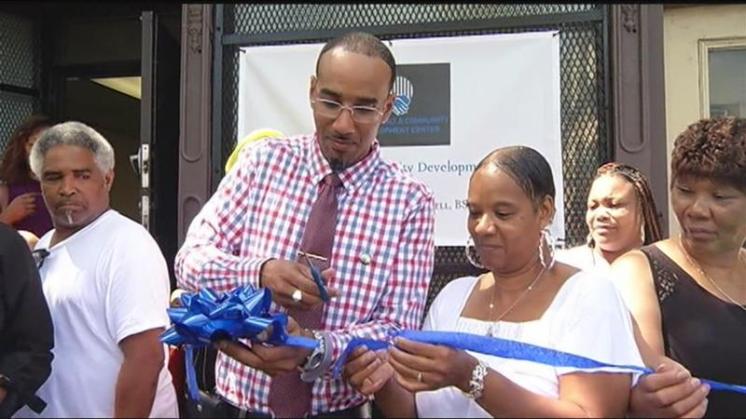 black man cutting blue ribbon in front of a store front